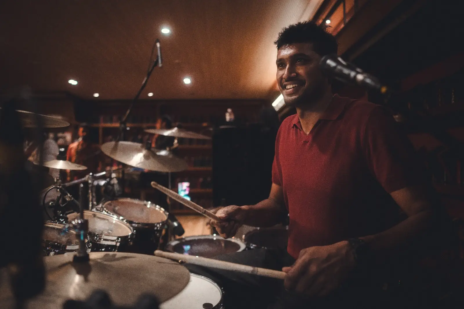 Yadhu smiling at the drums in a warmly lit venue